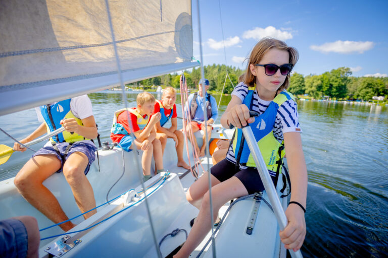 Dzieci na żaglówce uczą się żeglować. Letnia przygoda na wodzie.