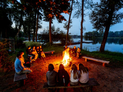 Ognisko nad jeziorem. Grupa przyjaciół siedzi przy ognisku, ciesząc się wieczorem.
