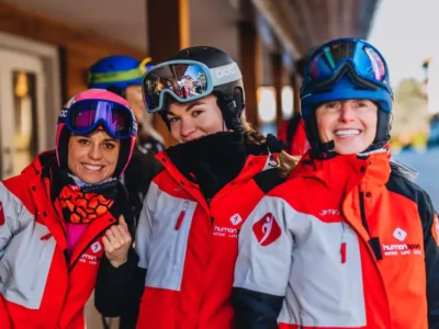 Trzy narciarki w czerwonych kurtkach i kaskach uśmiechają się do aparatu.