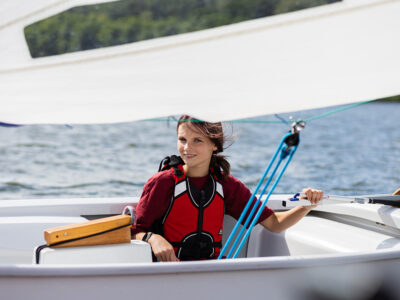 Dziewczynka na żaglówce w kamizelce ratunkowej. Żeglarstwo, sporty wodne, wakacje.