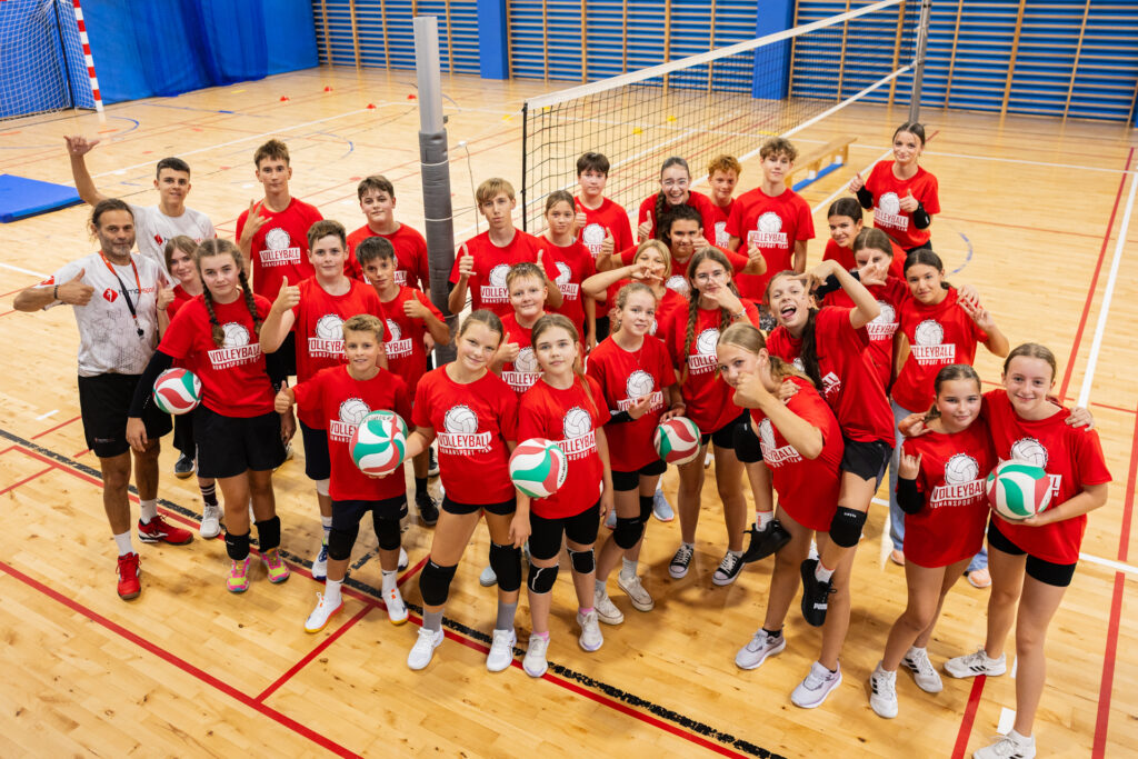 Młoda drużyna siatkarska w czerwonych koszulkach z piłkami do siatkówki, gotowa do gry.