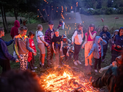 Dzieci pieką kiełbaski nad ogniskiem. Letnia przygoda i wspólne chwile.