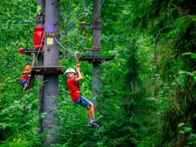 Chłopiec zjeżdża na tyrolce w parku linowym. Przygoda w lesie dla dzieci.