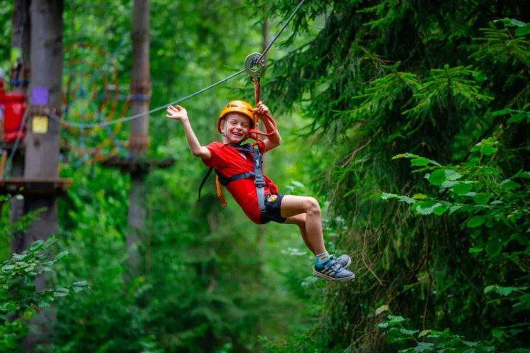 Chłopiec zjeżdża na tyrolce w parku linowym.