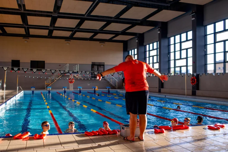 Instruktor pływania na brzegu basenu pokazuje dzieciom ćwiczenia podczas nauki pływania