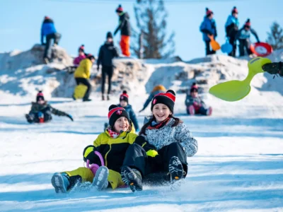 Dzieci zjeżdżają na sankach po śniegu. Radość z zimowych zabaw na świeżym powietrzu.