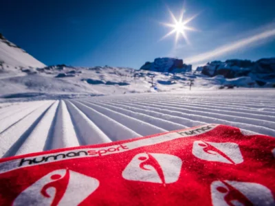 Czerwona chusta narciarska z logo na tle przygotowanego stoku narciarskiego.