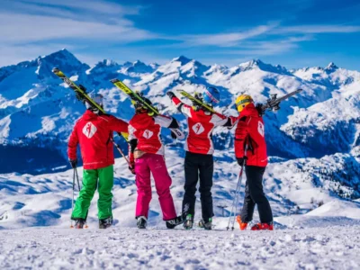 Narciarze w czerwonych kurtkach z nartami na ramionach podziwiają zimowy krajobraz gór.