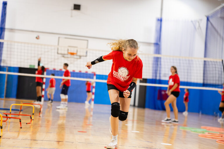 Dziewczynka w czerwonej koszulce ćwiczy siatkówkę na hali sportowej.