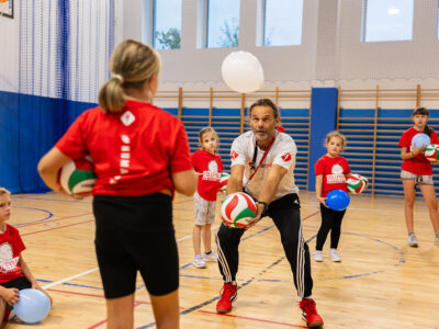 Trener siatkówki z dziećmi na sali gimnastycznej. Nauka gry w siatkówkę.