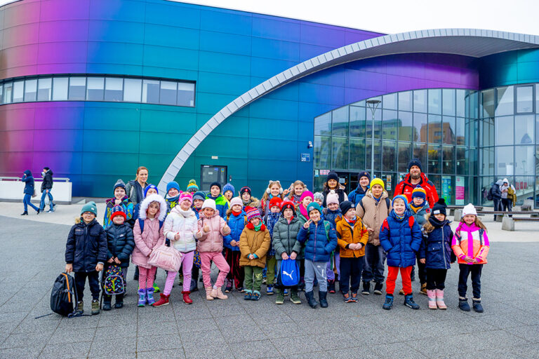 Dzieci i dorośli przed kolorowym budynkiem. Wycieczka szkolna, zimowy dzień.
