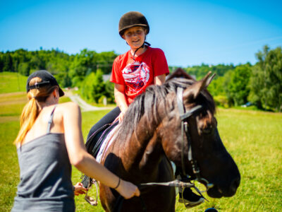Dziewczynka w kasku na koniu, nauka jazdy konnej, wakacje na wsi.