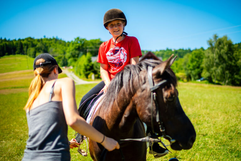 Dziewczynka w kasku na koniu, nauka jazdy konnej, wakacje na wsi.