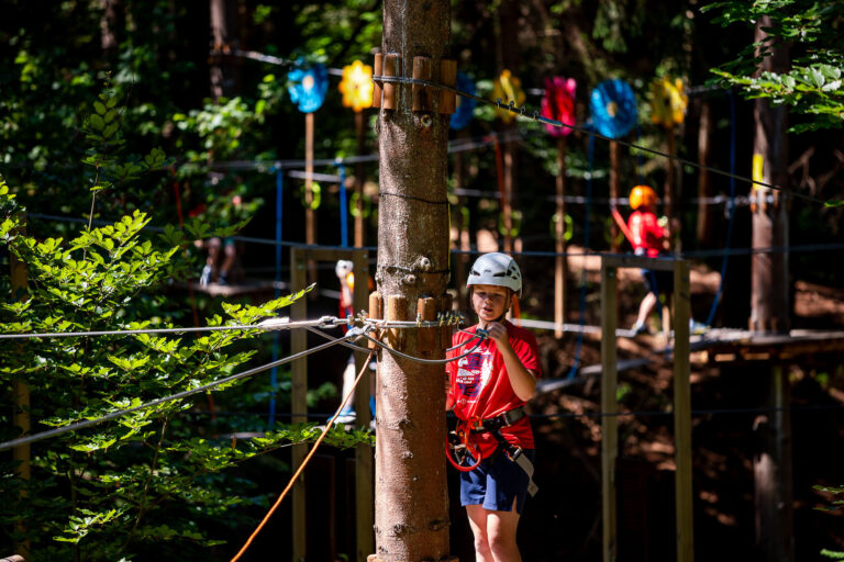Dziecko w kasku na parku linowym, przygotowuje się do przejścia trasy. Bezpieczeństwo i zabawa na wysokości.
