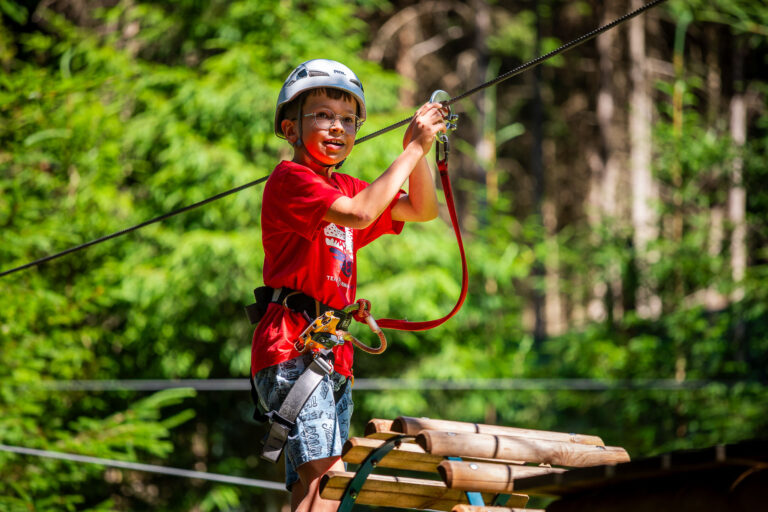 Chłopiec w kasku i czerwonej koszulce na parku linowym, gotowy do zjazdu.