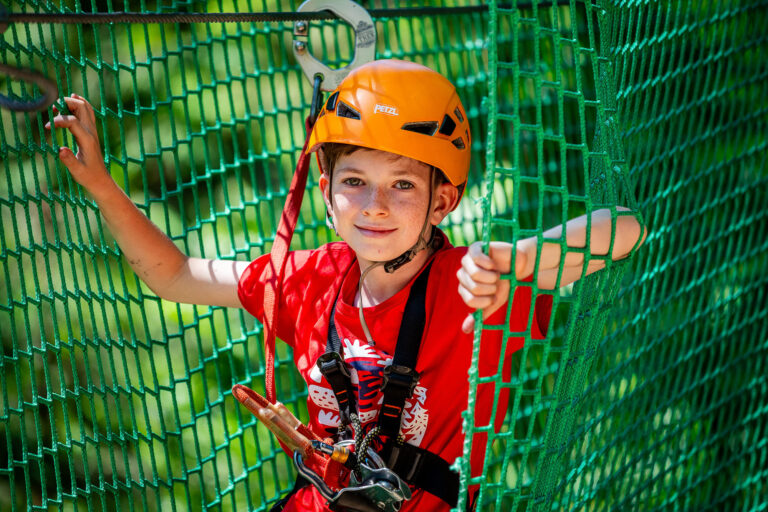 Chłopiec w kasku na parku linowym. Przygoda i zabawa na wysokości.