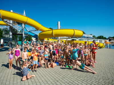 Dzieci na basenie z żółtą zjeżdżalnią. Radosna grupa na wakacjach.
