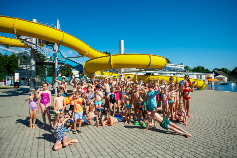 Dzieci na basenie z żółtą zjeżdżalnią. Radosna grupa na wakacjach.
