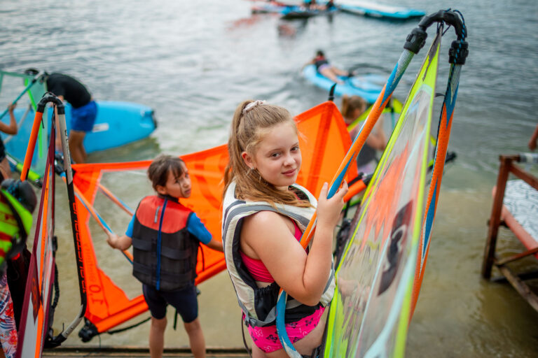 Dzieci przygotowują się do windsurfingu. Wodne sporty dla najmłodszych.