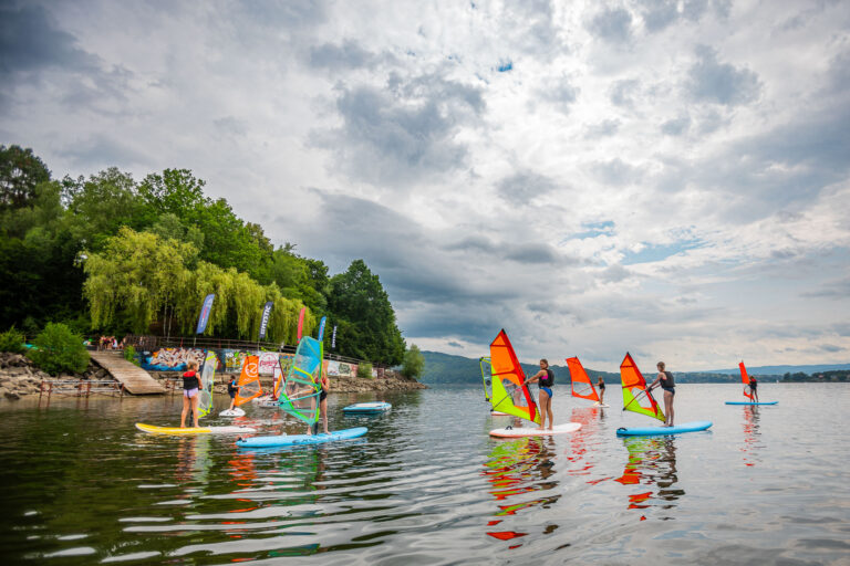 Zajęcia z windsurfingu na jeziorze. Ludzie uczą się pływać na deskach z żaglami.