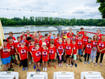 Dzieci w czerwonych koszulkach na plaży nad jeziorem.