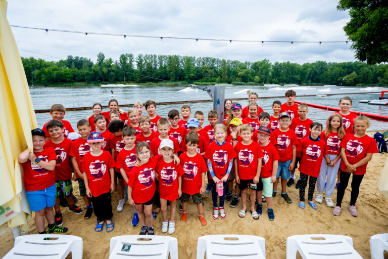 Dzieci w czerwonych koszulkach na plaży nad jeziorem.
