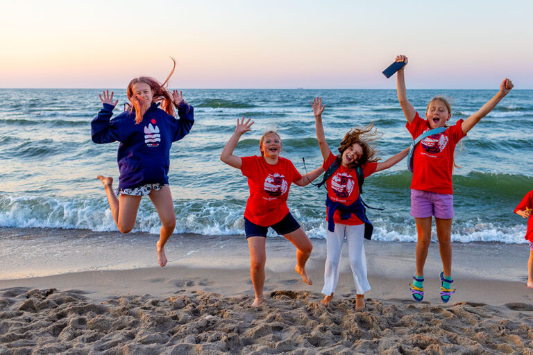 Radosne dzieci skaczą na plaży o zachodzie słońca. Wakacje, morze, szczęście.