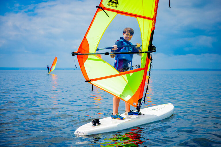 Chłopiec na desce windsurfingowej, słońce, wiatr i woda. Idealny dzień na sport wodny!
