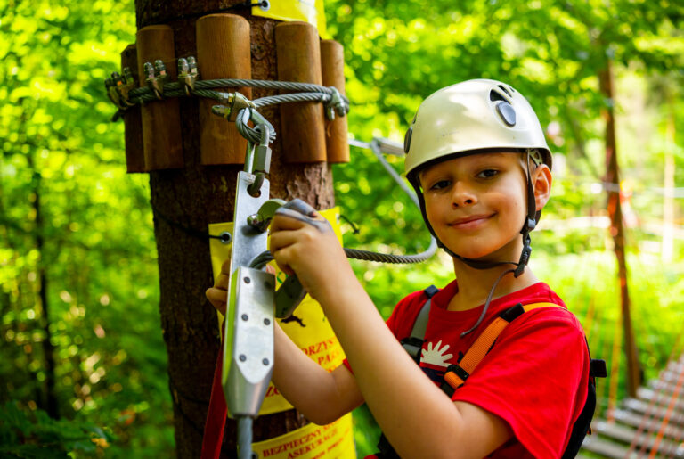 Chłopiec w kasku na parkingu linowym, gotowy na przygodę w lesie.