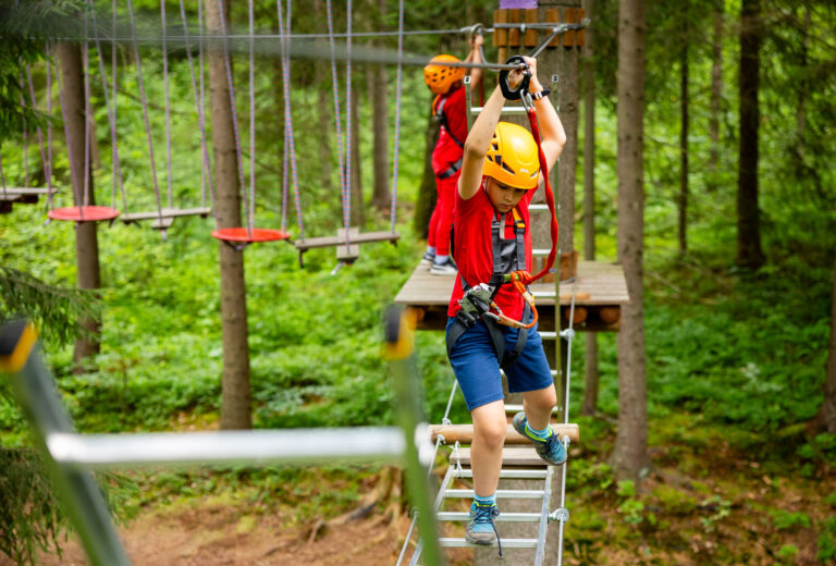 Dzieci na parku linowym w lesie. Przygoda i zabawa na wysokościach.