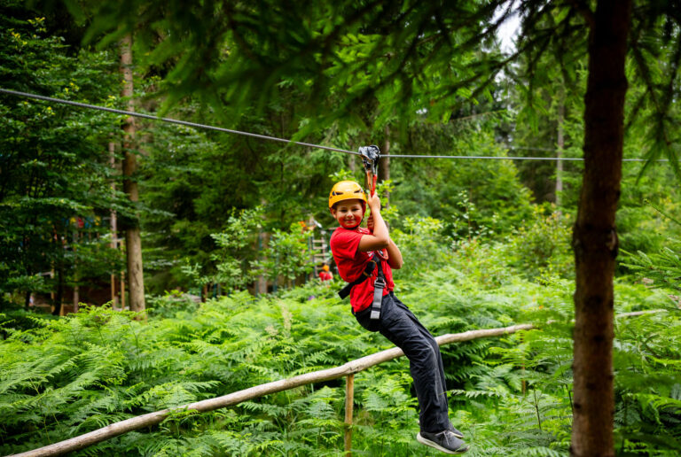 Chłopiec na zjeżdżalni tyrolskiej w lesie. Przygoda i zabawa na świeżym powietrzu.