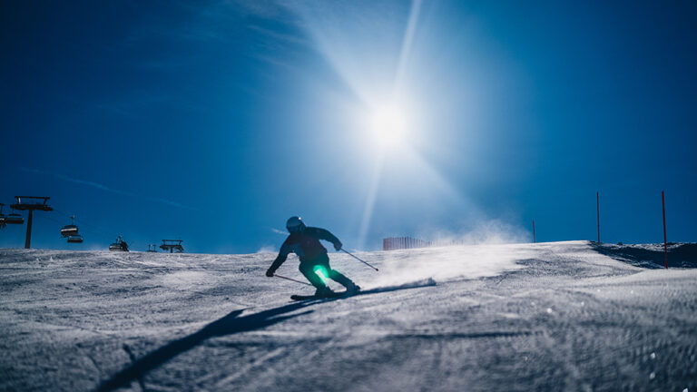 Narciarz zjeżdża po ośnieżonym stoku w słoneczny dzień.