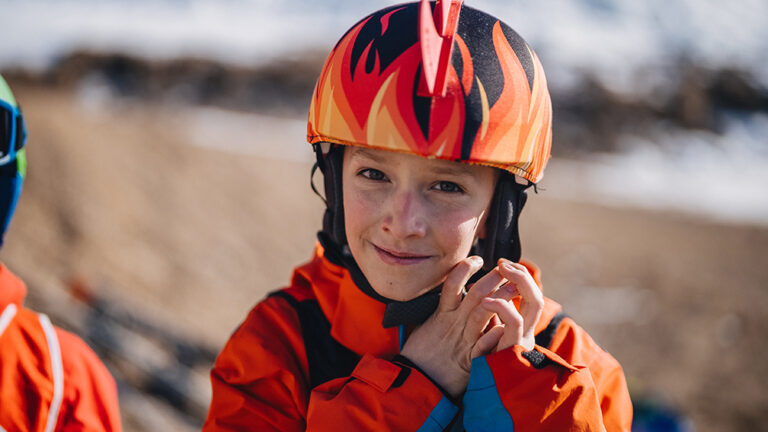 Uśmiechnięty chłopiec w pomarańczowej kurtce i kasku z płomieniami. Idealny na narty!