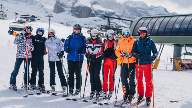 Grupa narciarzy w kolorowych strojach pozuje do zdjęcia na stoku narciarskim.