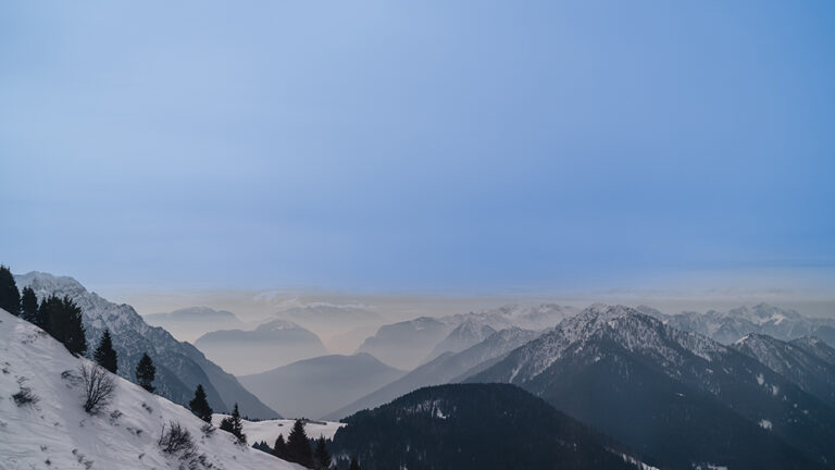 Zimowy krajobraz górski z ośnieżonymi szczytami i sosnami na pierwszym planie.