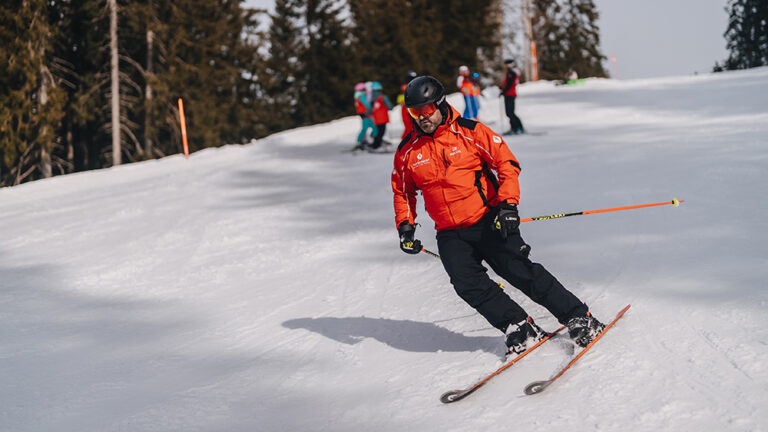 Narciarz w pomarańczowej kurtce zjeżdża po stoku.