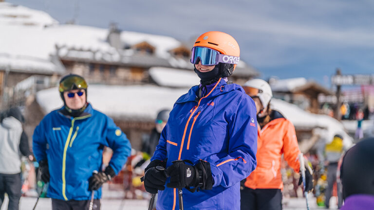 Narciarze w kolorowych kurtkach i kaskach na stoku narciarskim.