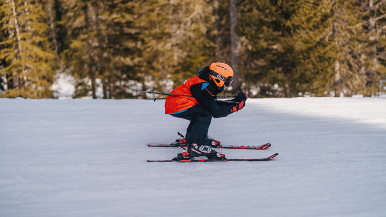 Dziecko na nartach w pomarańczowej kamizelce z kaskiem, zjazd na stoku.