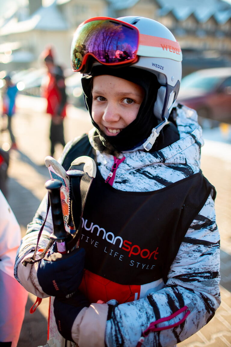 Uśmiechnięta narciarka w kasku i goglach, gotowa na stok. Narty i kijki.