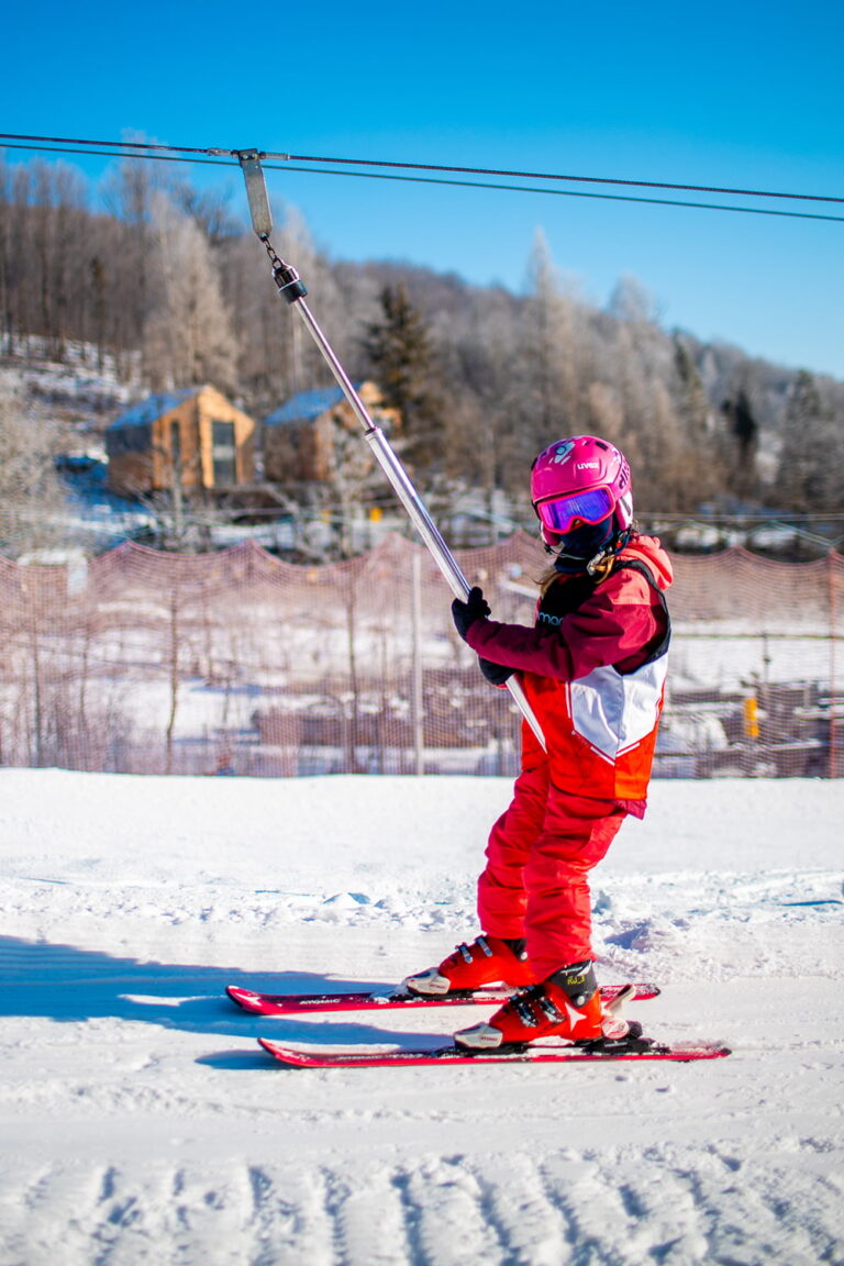 Dziecko na nartach korzysta z wyciągu orczykowego na stoku narciarskim.