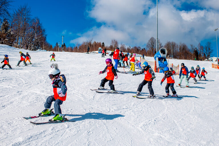 Dzieci uczą się jeździć na nartach na stoku.