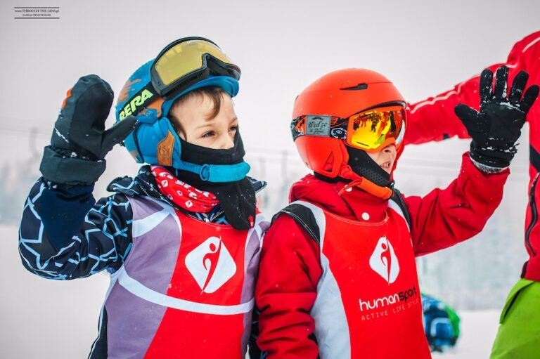 Dzieci w strojach narciarskich, kaskach i goglach pozdrawiają. Narciarstwo, zimowy sport.